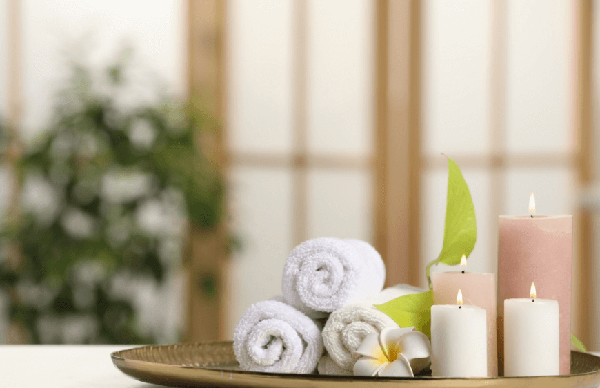 Spa kompozisyonu,beyaz bir masanin uzerinde yanan mumlar,yesil yapraklar ve havlular